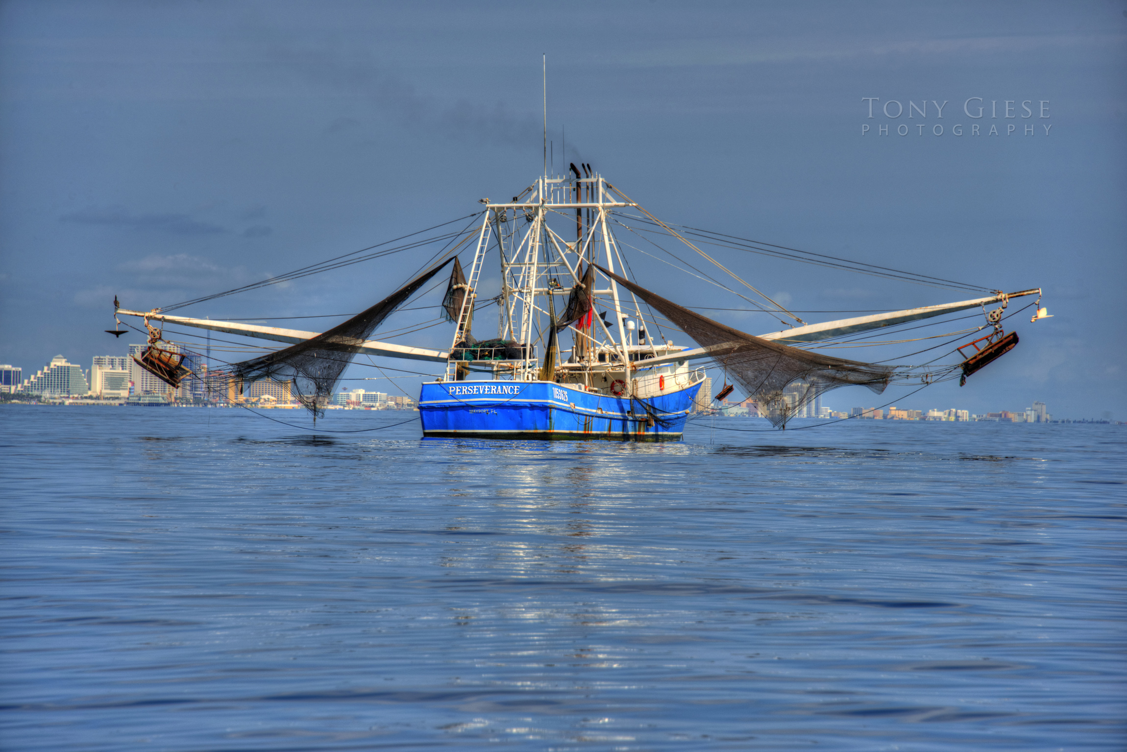 Shrimp boat on blue water with nets up offshore of Daytona Beach blue water skyline.
